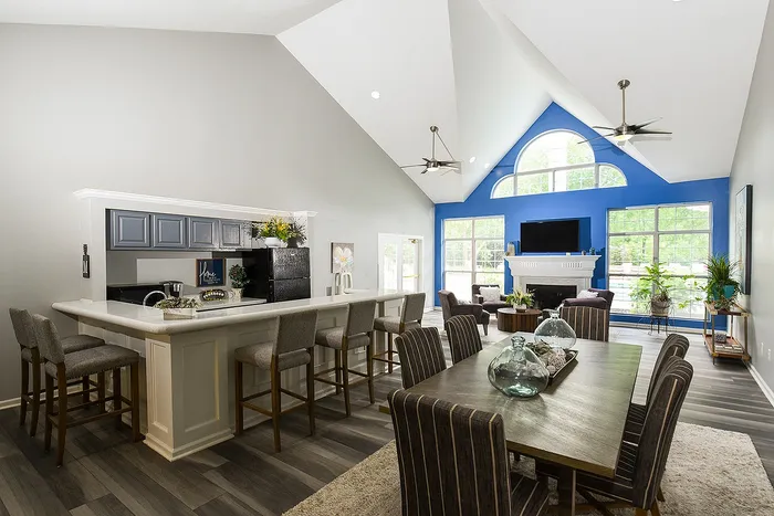 Elegant open-plan living and dining area with high vaulted ceilings, modern kitchen island with bar stools, and a cozy seating space by large windows and a stylish fireplace.