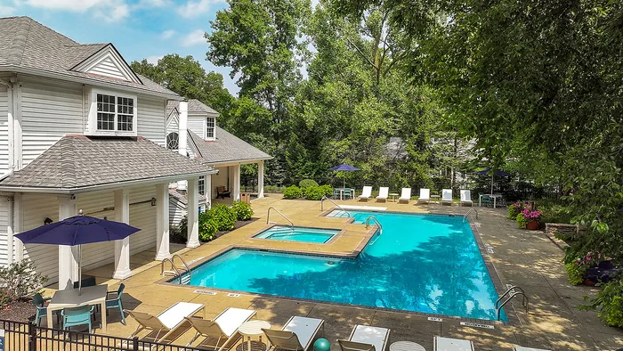 Charming apartment complex featuring a refreshing outdoor pool with lounge chairs, surrounded by lush greenery and elegant architecture.