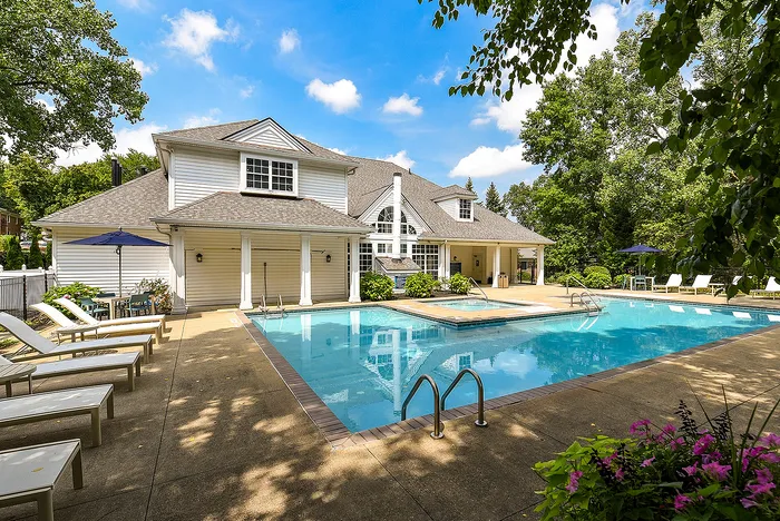 Luxurious residential pool area with spacious patio, elegant white house, and vibrant garden, perfect for relaxation and entertainment.