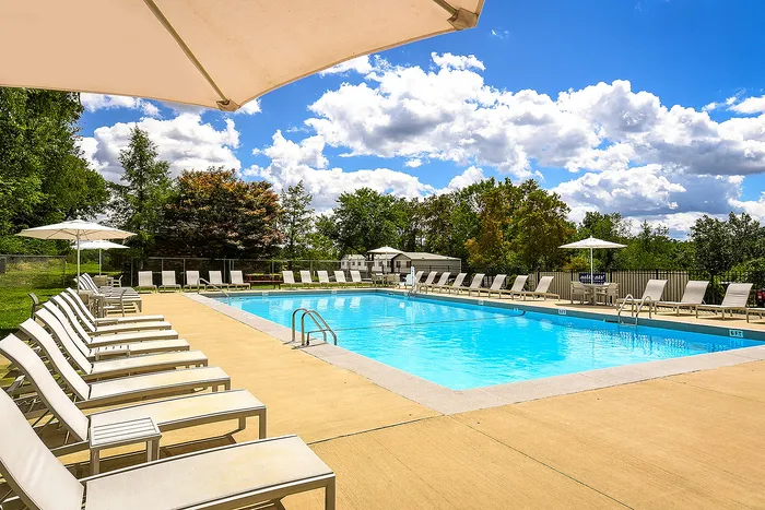 Inviting outdoor swimming pool surrounded by elegant lounge chairs and vibrant greenery under a clear blue sky.