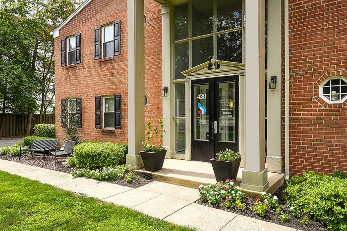 Charming brick apartment entrance with lush landscaping and welcoming seating area.
