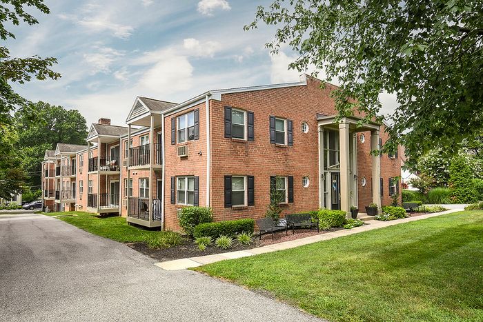Charming brick apartment complex surrounded by lush greenery and vibrant landscaping, featuring private balconies and a welcoming entrance.