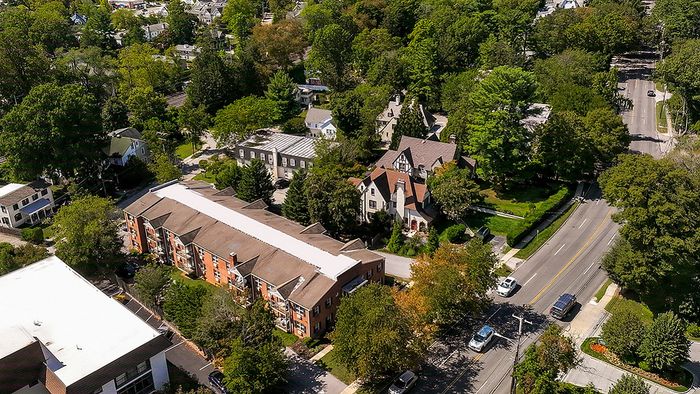 Charming aerial view of a picturesque neighborhood showcasing lush greenery, elegant homes, and a vibrant residential building near a tree-lined street.