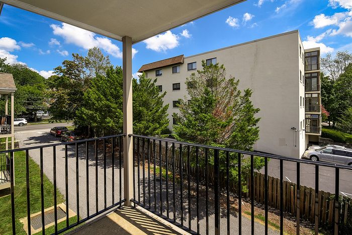 Inviting balcony view with lush greenery and modern apartment building under a bright blue sky.