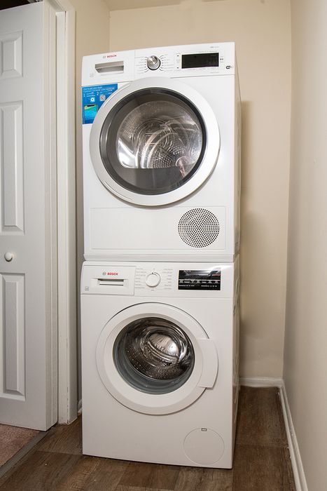 Modern apartment utility room featuring a sleek, space-saving stacked Bosch washer and dryer on wood flooring.