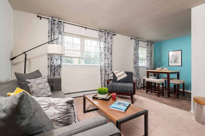 Bright and inviting living room with modern decor, featuring cozy seating, stylish coffee table, and a chic dining area against a calming blue accent wall.