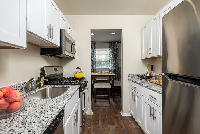 Modern kitchen with sleek white cabinets, stainless steel appliances, and granite countertops leading to a cozy dining nook.