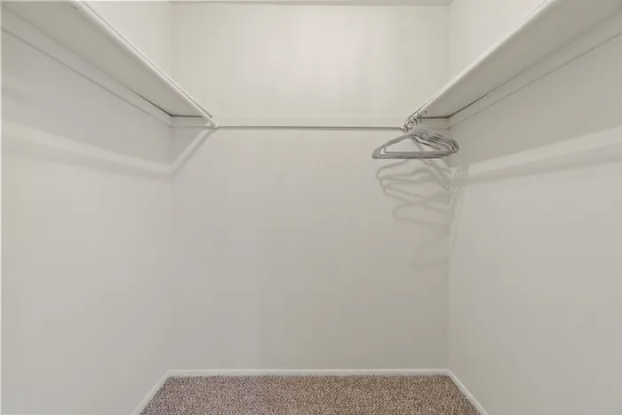 Spacious walk-in closet with bright white walls and cozy carpet, featuring a sleek hanging rod and hangers.