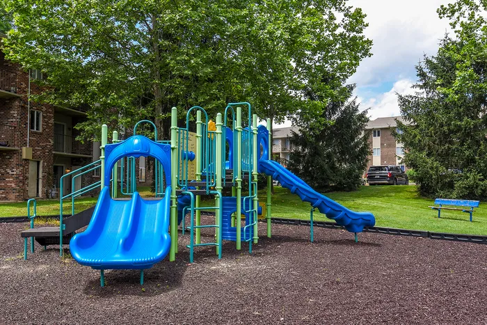 Charming outdoor playground with vibrant blue slides and climbing structures surrounded by lush greenery, perfect for family fun.