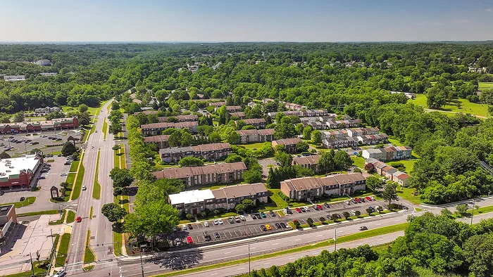 Aerial view of a picturesque apartment community surrounded by lush greenery, showcasing convenient access to main roads and nearby amenities.