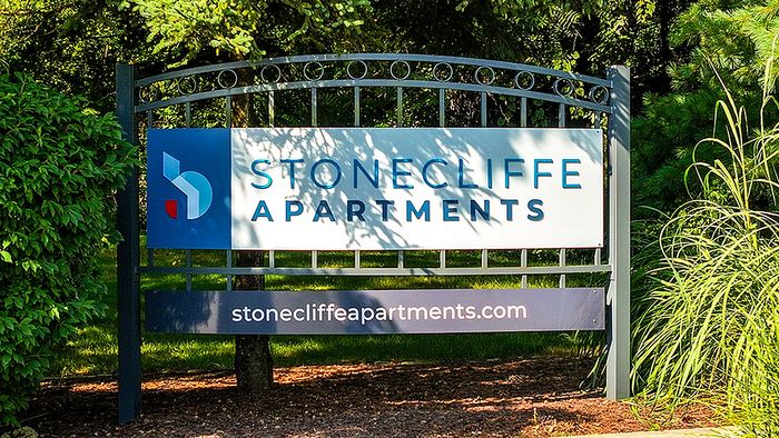 Inviting sign for Stonecliffe Apartments, nestled amidst lush greenery, promising tranquil living.