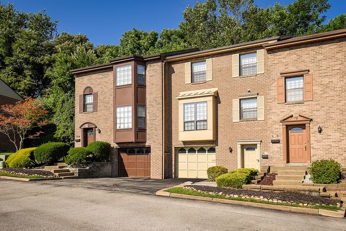 Charming townhouse with brick facade and bay windows, nestled in a lush green setting with manicured shrubs.