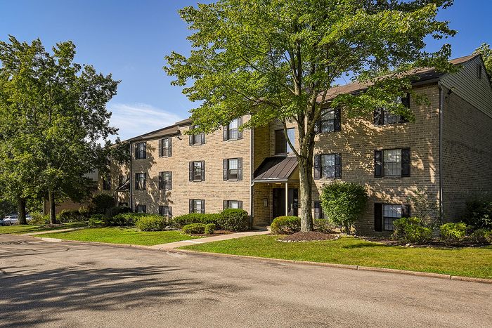 Charming brick apartment building surrounded by lush greenery and serene trees, offering a peaceful residential setting.