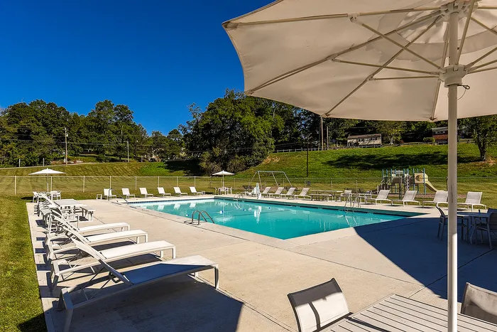 One-Bedroom Apartments in Bethel Park, PA - Lindenbrooke - Swimming Pool with Expansive Sundeck, Lounge Chairs, Tables and Chairs with Umbrellas, and Surrounding Manicured Landscape.