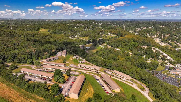 Scenic aerial view of a peaceful residential complex nestled in lush green surroundings with picturesque hill views and clear blue skies.