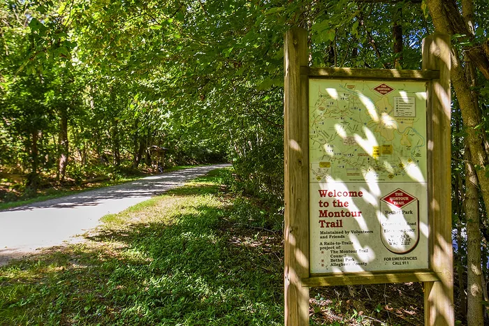 Scenic entrance to Montour Trail with lush greenery and informational trail sign, perfect for outdoor enthusiasts.