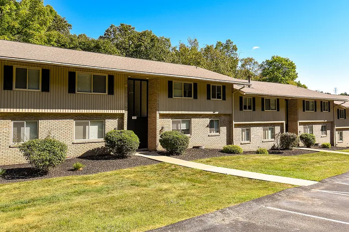 Charming two-story apartment building with modern brick façade, surrounded by lush greenery and well-manicured lawns under a clear blue sky.