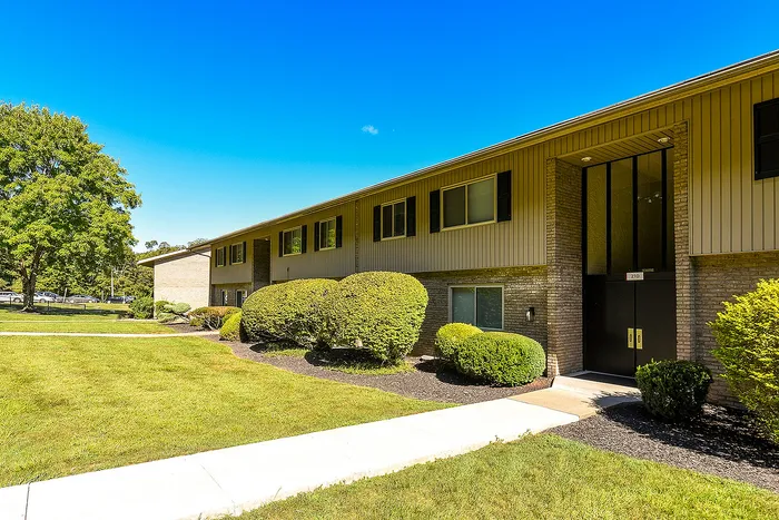 Charming two-story apartment building with manicured greenery and a bright blue sky backdrop.