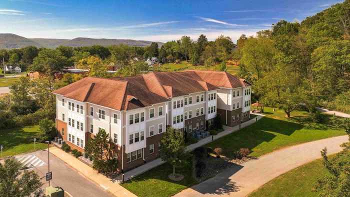 Beautiful aerial view of a modern apartment building surrounded by lush greenery and scenic mountains, offering a tranquil and picturesque living environment.