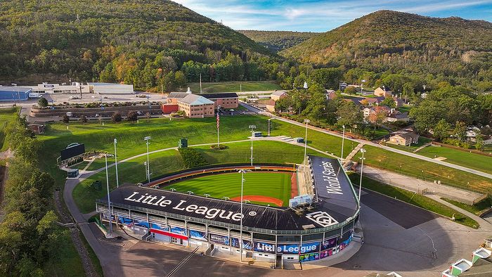 Aerial view of a picturesque Little League baseball stadium nestled among lush green hills, showcasing vibrant landscape and community charm.