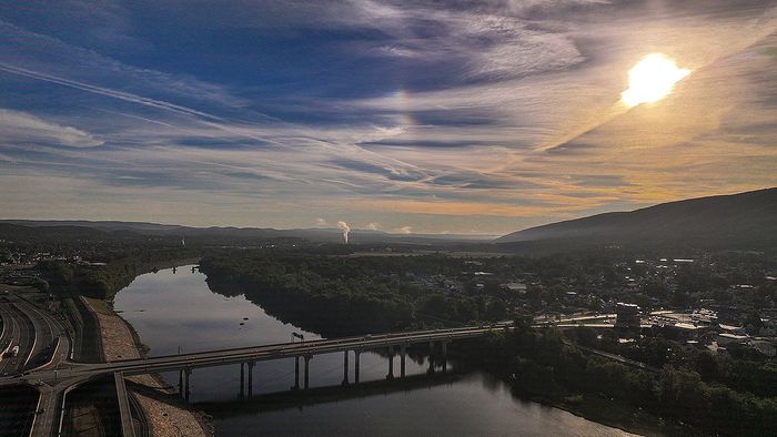 Breathtaking aerial view of a serene riverside cityscape with a stunning sunset illuminating the sky and a bridge spanning the tranquil water.