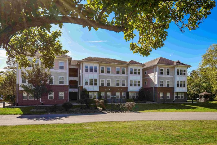 Charming three-story apartment building with classic brick and siding exterior, surrounded by lush greenery and a peaceful outdoor setting.