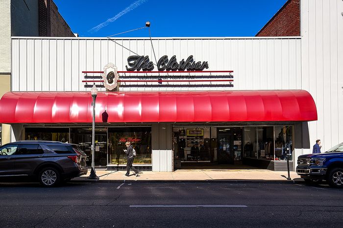 Charming storefront with a vintage red awning, showcasing 'The Clothier' sign, inviting pedestrians in for a classic shopping experience.