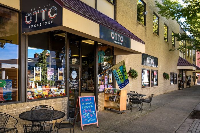 Charming bookstore storefront with inviting outdoor tables, vibrant shop local signage, and a colorful display of books.