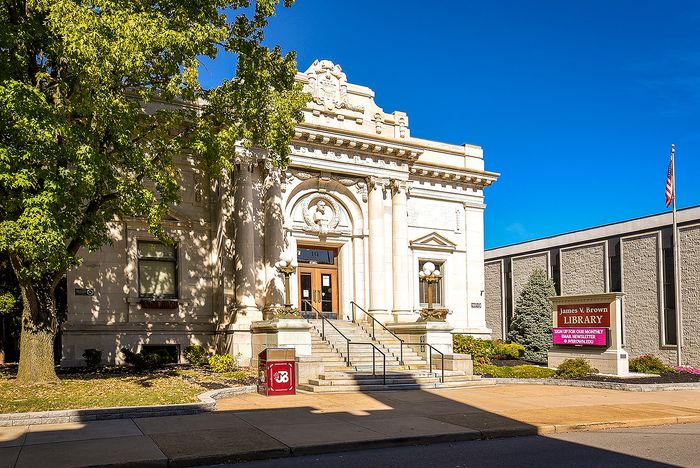 Elegant historic library entrance with grand columns and lush greenery, bathed in vibrant sunlight.