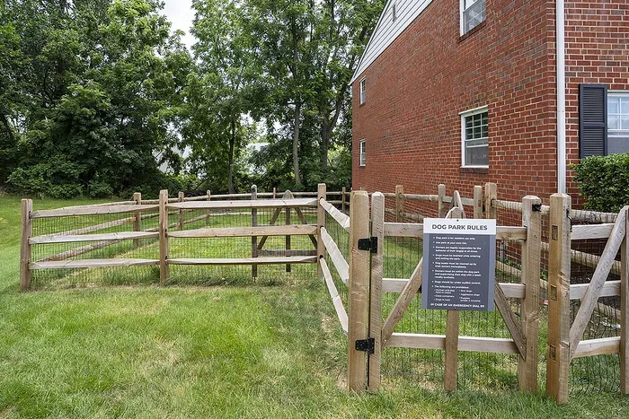 Inviting dog park with wooden fencing adjacent to a brick apartment building, surrounded by lush greenery.