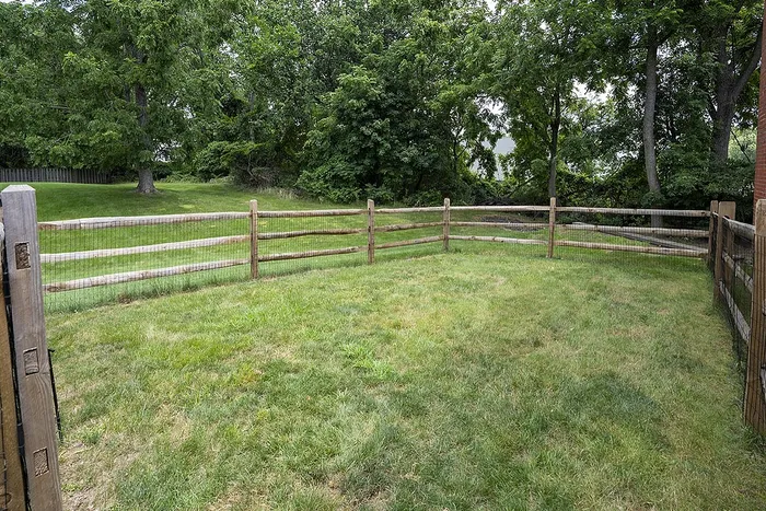 Charming backyard with lush green grass and rustic wooden fence, surrounded by mature trees for a serene escape.