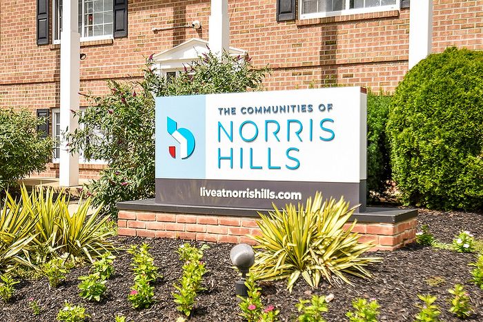 Charming entrance sign for The Communities of Norris Hills, surrounded by lush greenery and vibrant plants.