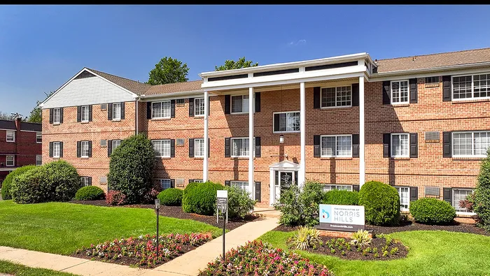 Charming brick apartment building with classic architecture, vibrant landscaped gardens, and welcoming entrance at Norris Hills.