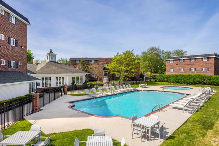Charming apartment complex featuring a pristine outdoor pool, surrounded by luxurious sun loungers and lush greenery, offering a perfect oasis for relaxation.