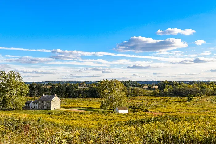 Charming stone house amidst a vast lush landscape under a vibrant blue sky, perfect for tranquil country living.