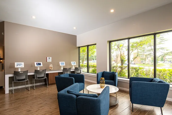 Modern community lounge with comfortable blue seating, large windows, and a tech-friendly workspace in a bright, inviting environment.