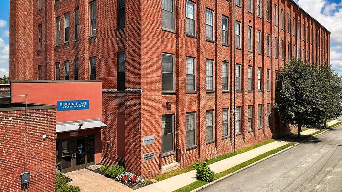 Charming red-brick apartment building with lush greenery at Ribbon Place, featuring large windows and inviting entrance.