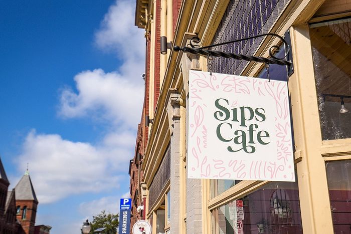 Charming Sips Cafe sign with elegant lettering, set against a vibrant blue sky backdrop.
