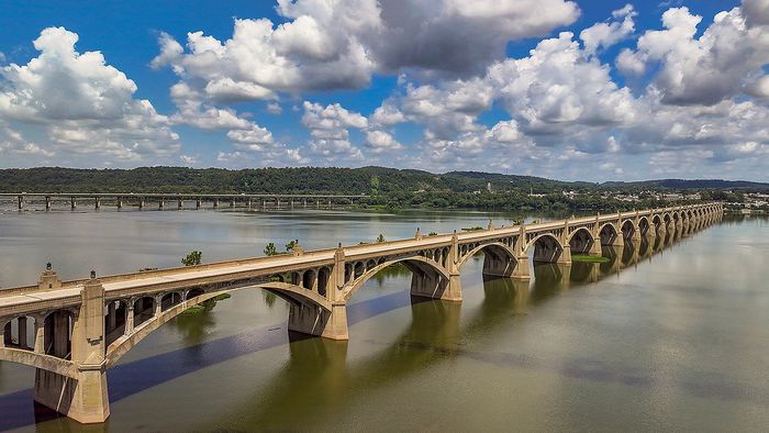 Magnificent arched bridge spanning serene waters under a vibrant sky with lush green hills in the background.