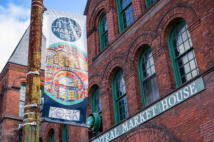 Charming historic building with red brick facade and green-framed windows; vibrant Market District banner adds colorful flair.