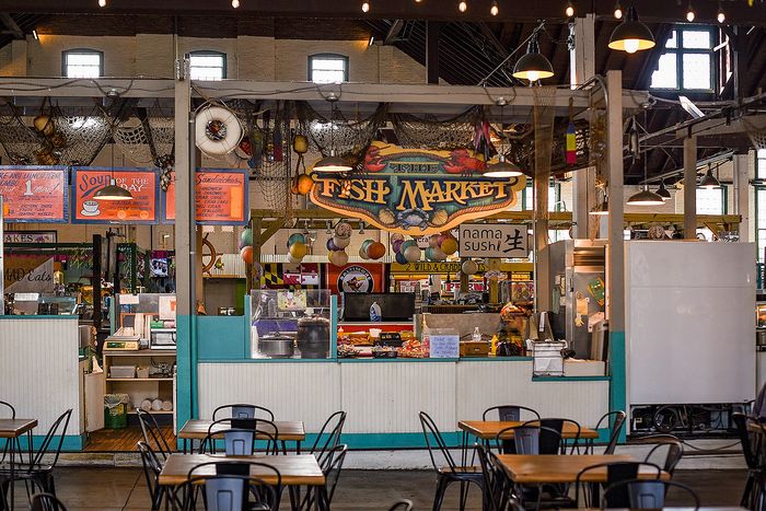 Vibrant indoor fish market featuring a variety of seafood stalls, colorful signage, and cozy dining tables.