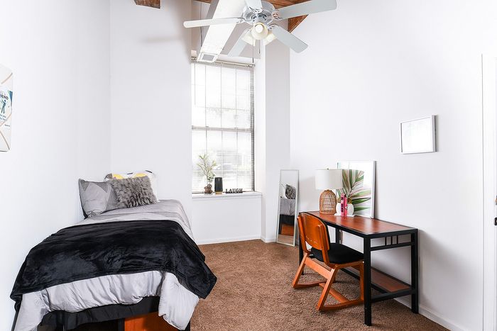 Bright and inviting bedroom with cozy bed, modern desk, and ceiling fan, perfect for study and relaxation.