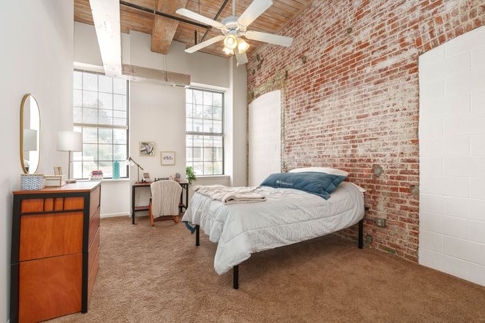 Charming bedroom with exposed brick wall, large windows, and stylish modern decor.