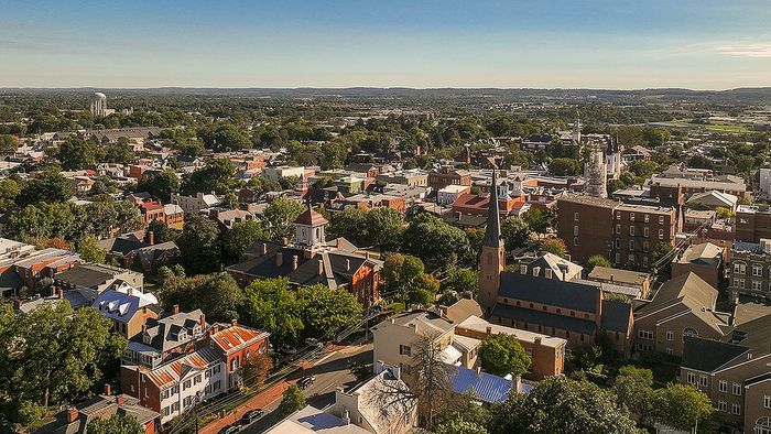 Breathtaking aerial view of a charming neighborhood, showcasing a blend of historic architecture and lush greenery under a clear blue sky.