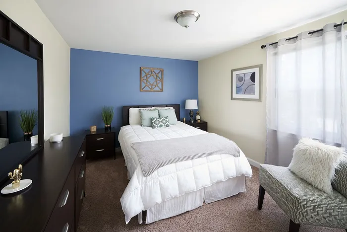 Inviting bedroom with modern accents, featuring a cozy bed, elegant decor, and plenty of natural light from a large window.