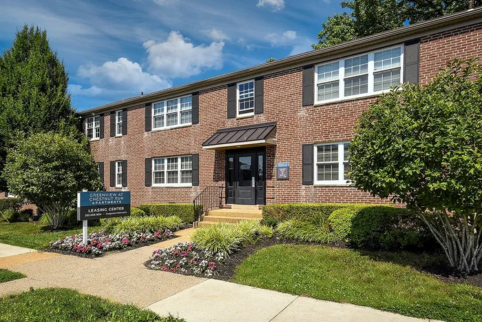 Inviting brick apartment building with well-manicured landscaping and vibrant flower beds under a clear, sunny sky at Greenview at Chestnut Run Apartments.