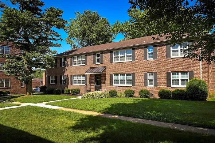 Charming brick apartment building nestled in lush greenery, offering a serene and inviting residential experience.