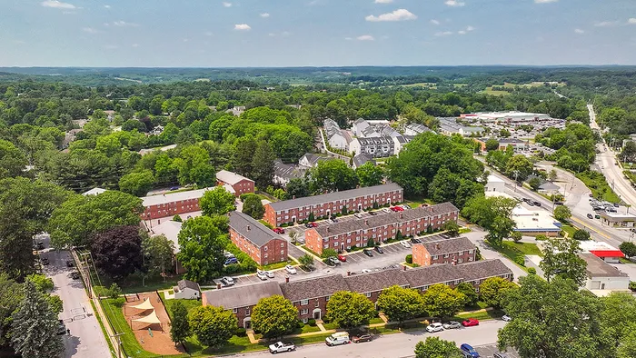Charming aerial view of a vibrant residential community, featuring classic brick apartment buildings surrounded by lush greenery, offering a serene suburban lifestyle.