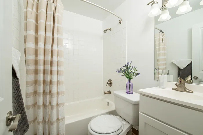 Bright and inviting bathroom featuring a modern bathtub, elegant vanity, and stylish lighting. Accented with a vibrant lavender arrangement for a touch of sophistication.