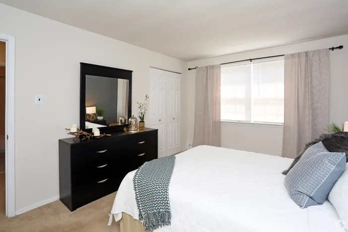 Bright and inviting bedroom with large window, stylish dresser, and cozy bed setup.
